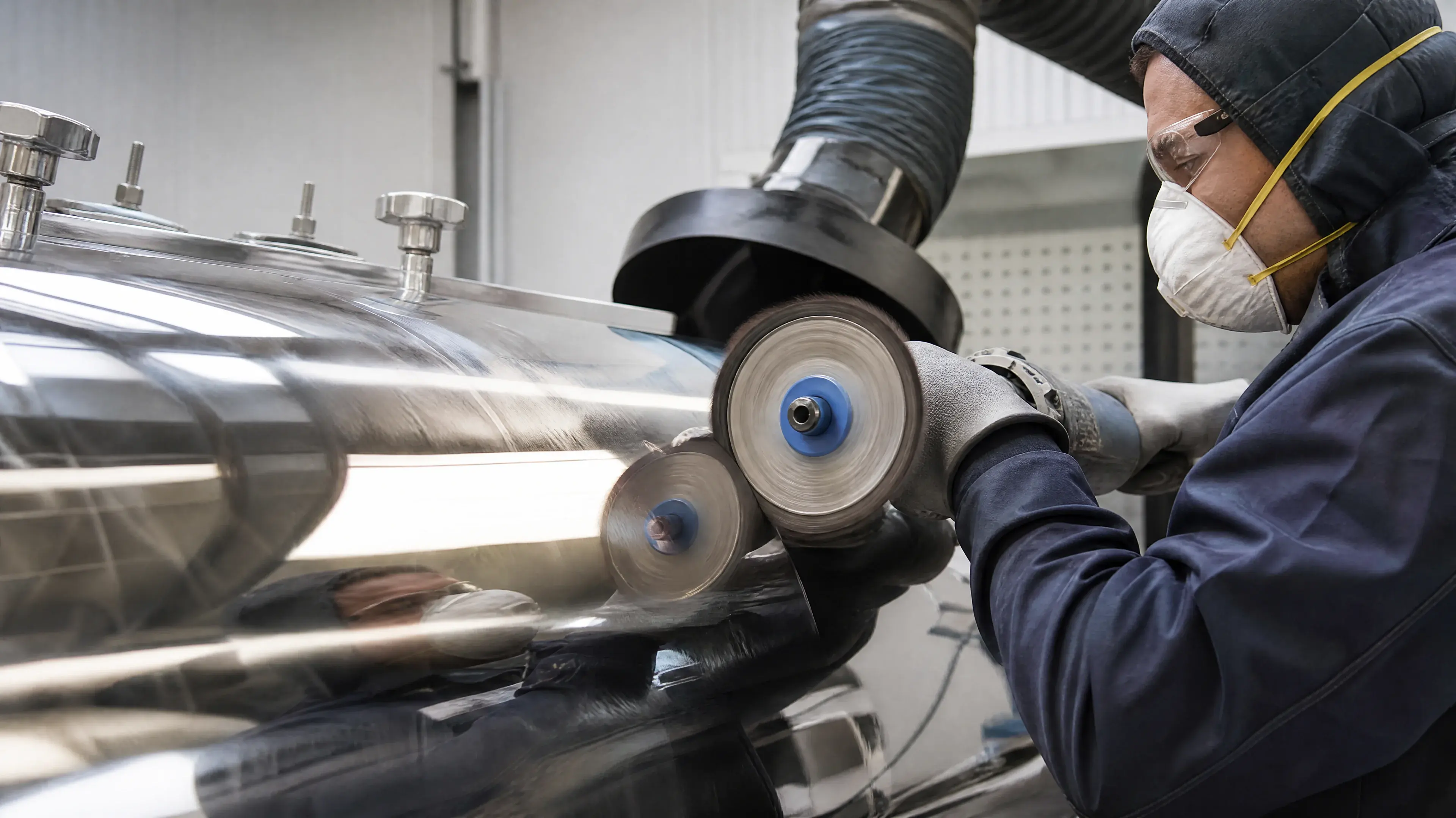 Technician polishing a reflective stainless surface in a controlled cell.