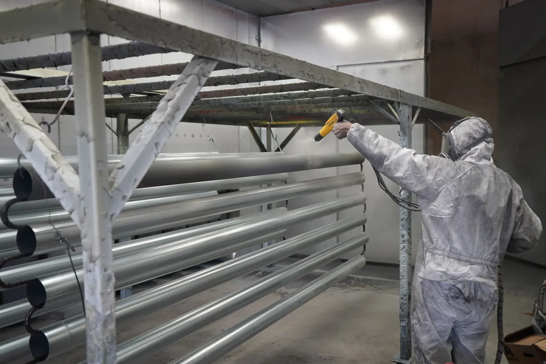 A technician applies powder coating to metal pipes in a workshop.